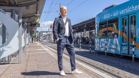 Mann im Anzug wartet an Haltestelle auf die Straßenbahn