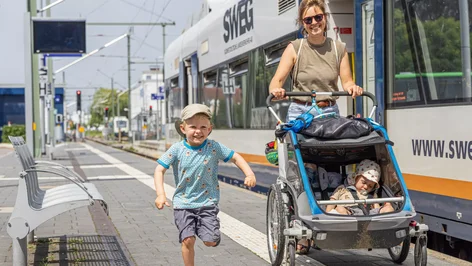 Frau mit Kinderwagen und kleinem Jungen läuft an S-Bahn-Haltestelle