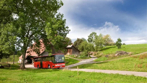 Roter Bus fährt an idyllischem Schwarzwaldhaus vorbei