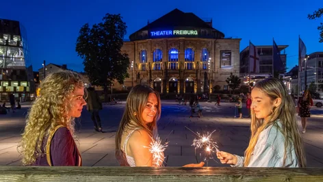 Frauen mit Wunderkerzen in der Dämmerung vor dem Theater Freiburg