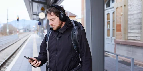 Junger Mann schaut auf sein Handy am Bahnhof