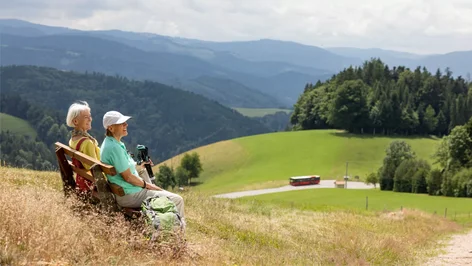 Zwei Wanderer sitzen auf einer Bank mit Blick in den Schwarzwald